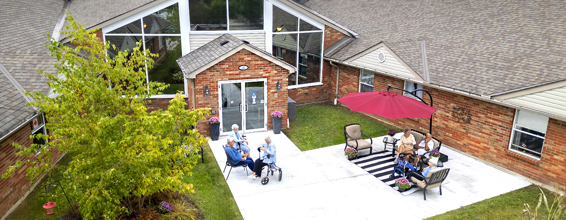 Residents enjoying a sunny afternoon on the patio, with some relaxing under an umbrella, at Atrium Retirement Residence in Orillia.