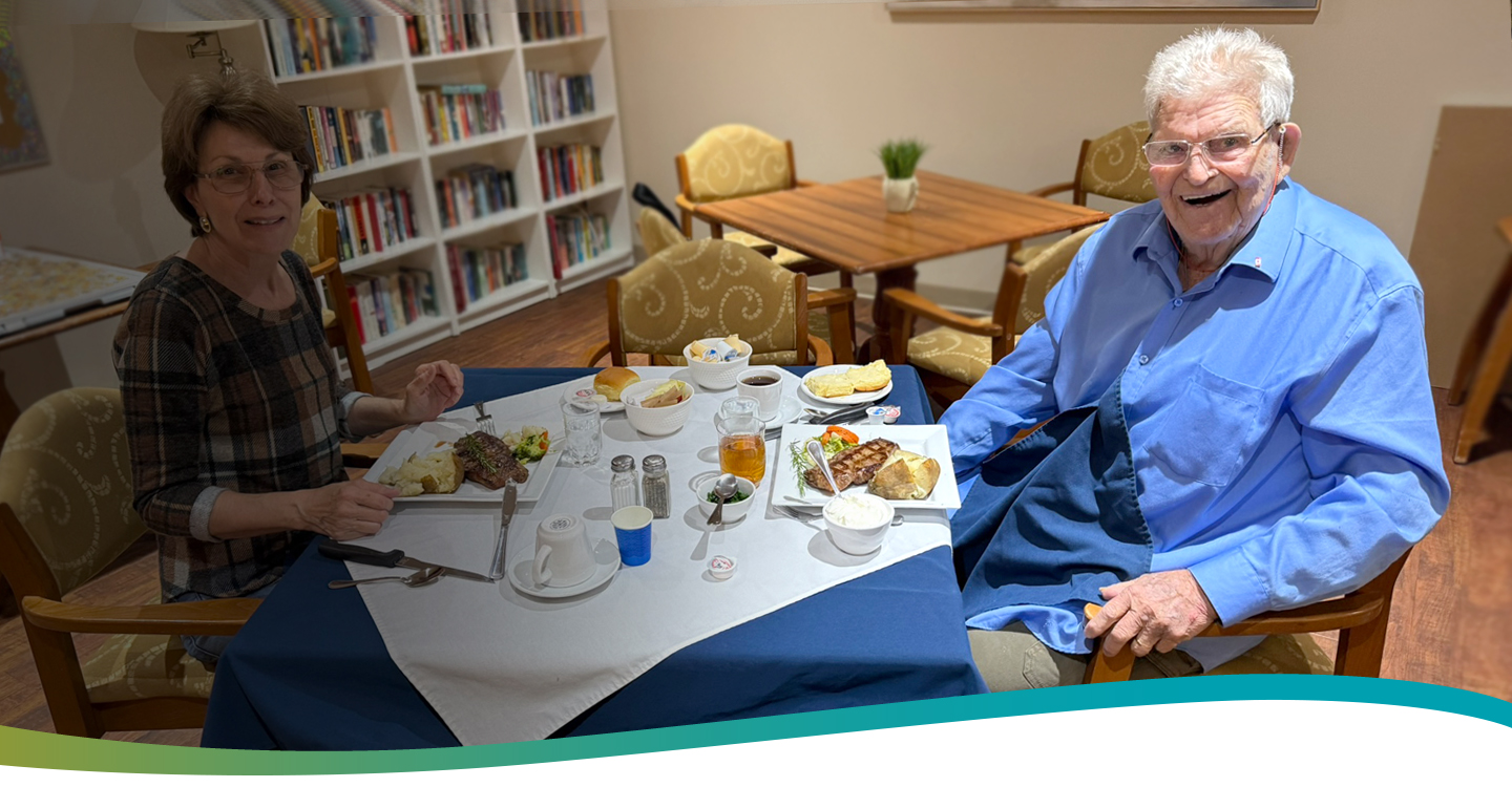 Resident Howard enjoying a private meal with a family member in the dining room at Atrium Retirement Residence in Orillia.
